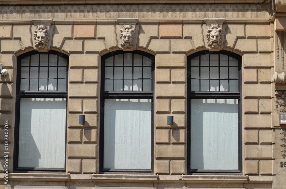 Obraz premium Facade of a historic building featuring three arched windows with ornate lion head sculptures and a classic stone design 