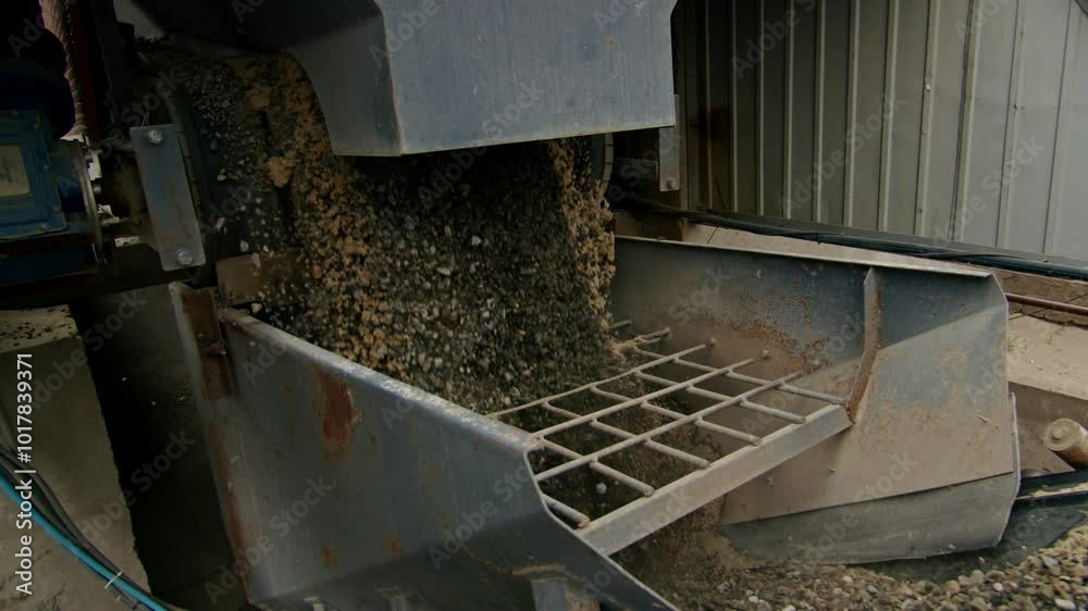 Gravel and sand being processed by industrial machinery in a manufacturing facility. Close-up of raw materials in production.