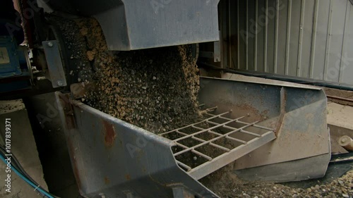 Gravel and sand being processed by industrial machinery in a manufacturing facility. Close-up of raw materials in production.