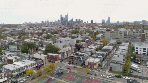 Aerial of Philadelphia Pennsylvania skyline with drone trucking left with buildings, row homes, and basketball court in foreground photo