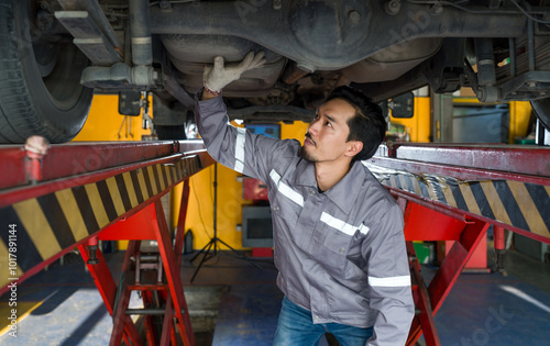 Young mechanic in gray uniform maintenance or inspection work on a vehicle that is raised on a lift.