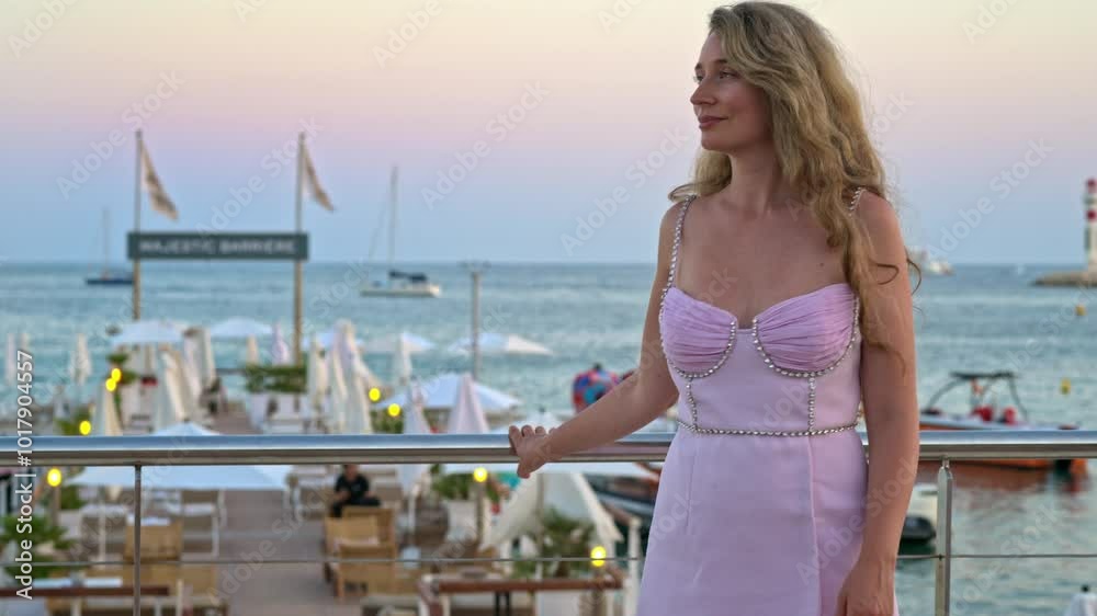 Woman in pink dress posing with the beach on the background in the evening in Cannes, France Woman in pink dress posing with the beach on the background in the evening in Cannes, France