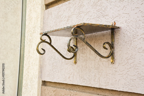 Forged Brackets with a memorial shelve for flowers. Bronze forged shelf with beautiful holders with scrolls and ornaments on the facade of a building. photo