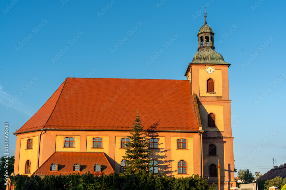 Historic church with a red roof and clock tower bathed in warm sunset light, set against a clear blue sky. High quality photo