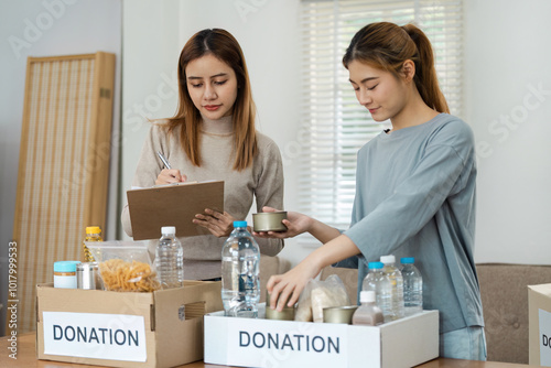 Two Women Organizing Donation Boxes with Food and Water in a Bright Room for Charity and Community Support photo