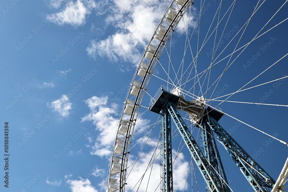 An Impressive Ferris Wheel Captured From Below With A Bright Blue Sky And Fluffy Clouds In The Background, Evoking A Sense Of Adventure And Delight. An Impressive Ferris Wheel Captured From Below With A Bright Blue Sky And Fluffy Clouds In The Background, Evoking A Sense Of Adventure And Delight.