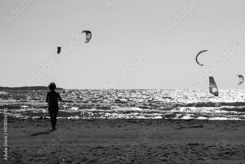 Foto in bianco e nero di una donna che cammina sulla spiaggia di Prassonissi a Rodi in Grecia, con wind surf e kite surf sullo sfondo photo