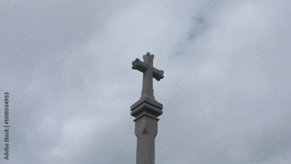 A stone cross monument rises against a cloudy sky, symbolizing faith and remembrance A stone cross monument rises against a cloudy sky, symbolizing faith and remembrance