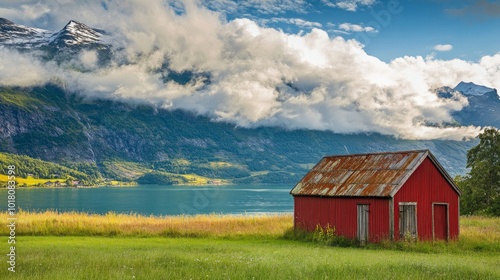 Gorgeous views of the colorful fjord. Blue clouds and a sunny morning. Cloud-covered mountains in the distance. In the verdant grass beside the sea lies a red fisherman's cottage. Scandinavian life.