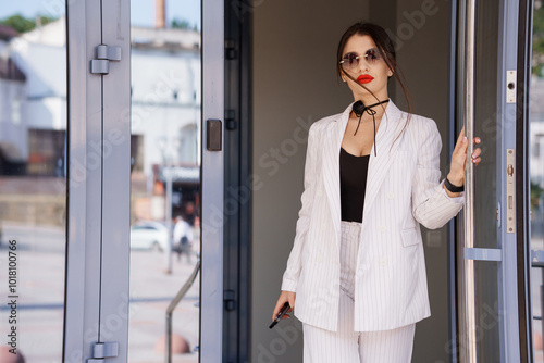 Stylish Businesswoman in Striped Suit Exiting Modern Glass Doors with Confidence