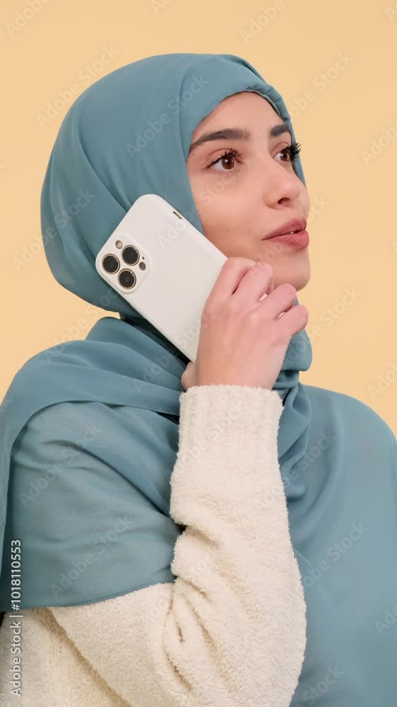 Smiley Arabian woman wearing hijab using smartphone for call with friends on beige background. Concept of a remote dialogue, negotiation. Vertical video. Smiley Arabian woman wearing hijab using smartphone for call with friends on beige background. Concept of a remote dialogue, negotiation. Vertical video.