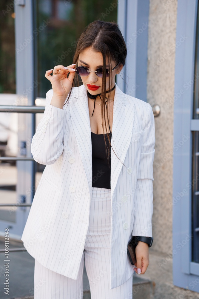 Fototapeta premium Chic Businesswoman in Pinstripe Suit with Sunglasses Posing Outdoors