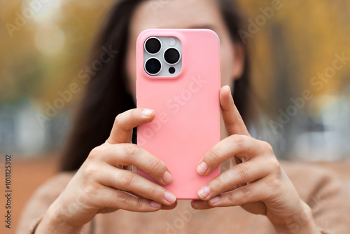 Closeup mobile phone in pink silicone case in girl hands, no face. Woman in fall city park make a photo on modern new smartphone. photo