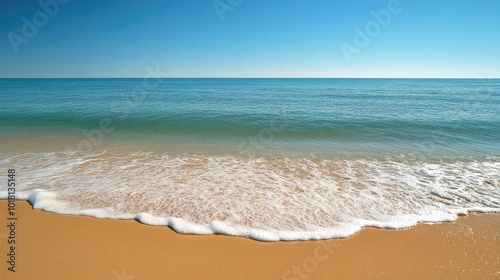 Wide view of gentle ocean waves rolling onto a sandy beach, with a clear sky and distant horizon