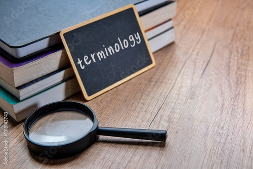 A chalkboard with the word "TERMINOLOGY" written on it is placed on a stack of textbooks on a wooden table. Copy space for text.