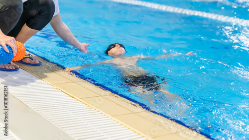 boy learning to swim in the pool with a trainer