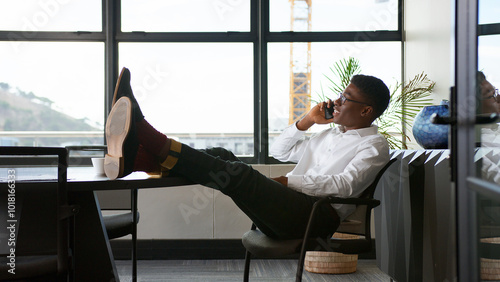 Young Businessman Relaxing Sitting In Office With Feet On His Desk In Office Talking On Mobile Phone