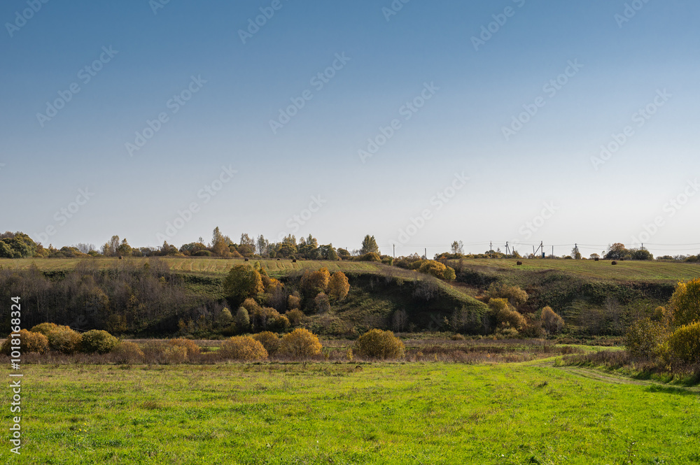 Fototapeta premium Autumn landscape with dirt road, field, far forest on hills.