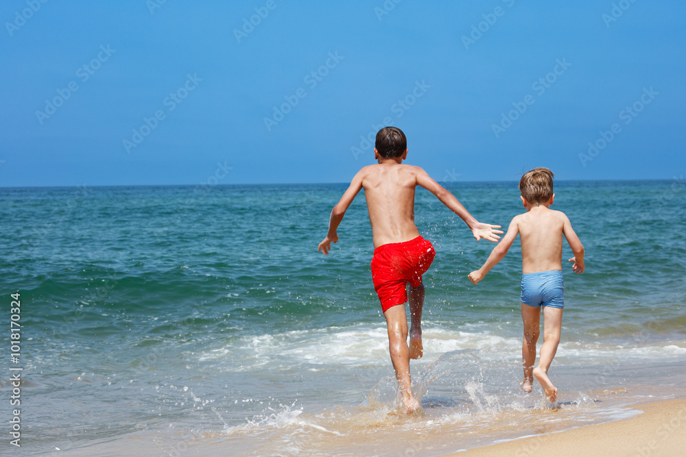 Two boys joyfully run into the ocean waves on a sunny beach day Two boys joyfully run into the ocean waves on a sunny beach day