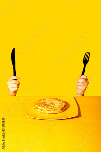 Hands holding a knife and fork over a meal against a yellow background photo