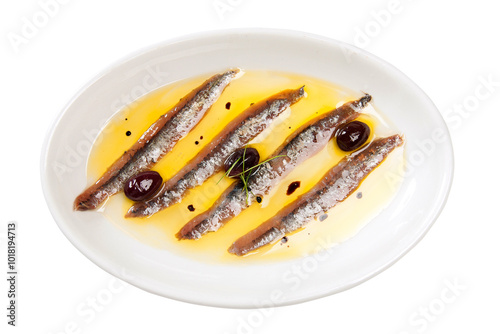 Overhead shot of a white plate with anchovies and black olives with rosemary in their oil