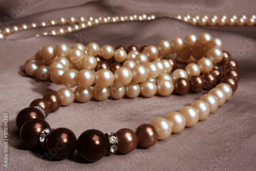 White and brown pearl necklace with diamond detail on a greyish fabric background photo