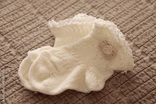 Knitted baby socks for christening with flower detail on brown fabric background photo