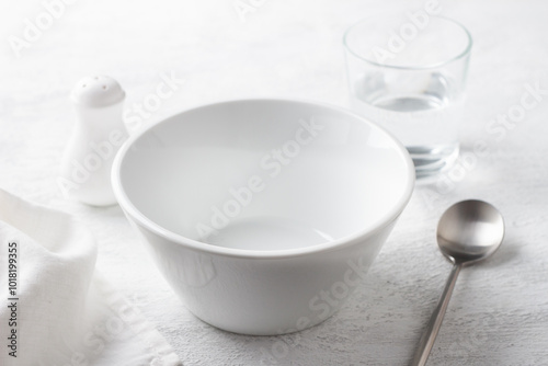 Simple table setting with white bowl, salt shaker, glass of water, and napkin on a gray surface