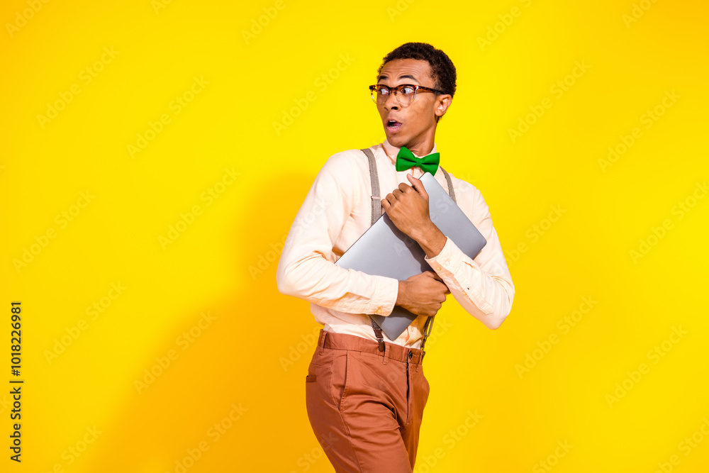 Photo of elegant young man hold netbook look empty space wear shirt bow tie isolated on yellow color background