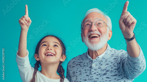 A grandfather with his granddaughter smiling and pointing upwards, light teal background.
family, happiness, smiling, joy, pointing, diversity, multiethnicity, togetherness. photo