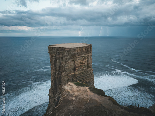 A rocky cliff overlooking the ocean with a storm brewing in the distance. The sky is dark and cloudy photo