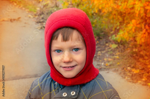 Portrait of happy cute little kid boy with autumn leaves background in colorful clothing. Funny child having fun in fall forest or park on cold day. High quality photo