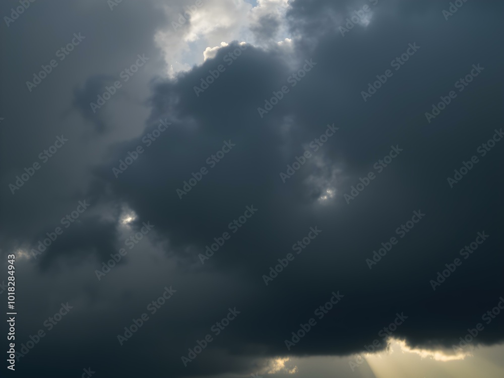 Obraz premium A moody sky with heavy gray clouds and soft sunlight peeking through, creating a dramatic contrast between light and shadow 