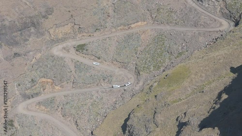 Wide aerial view of three offroad tour vehicles manoeuvring up the rugged Sani Pass