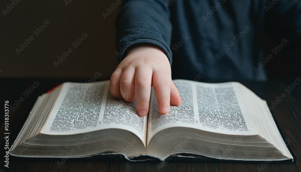 A child's small hand touching the center of an open Bible A child's small hand touching the center of an open Bible