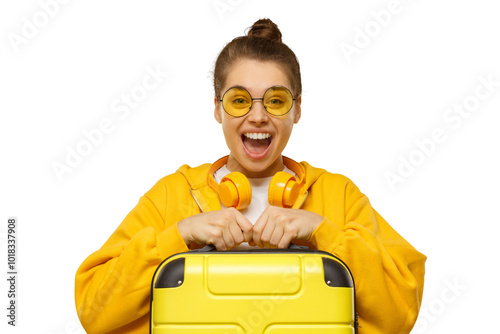 Happy excited girl wearing hoodie, yellow colored glasses and headphones around neck, holding travel suitcase, feeling ready for flight