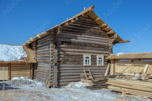 A wooden house made of rounded logs. Renovated rustic house built in the 19th century. Cracked dark logs of a wooden house. Flat boards near the house in the countryside.