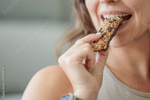 Portrait of a smiling young woman eating a protein bar with chocolate chips. Close up, copy space.