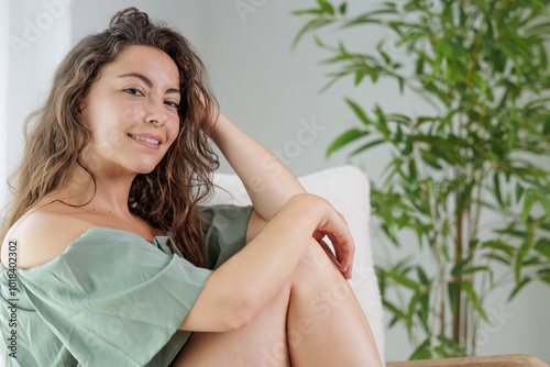 Portrait and close-up of a young woman smiling at the camera, she is relaxed and calm in the armchair at home.