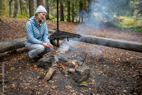 woman in the blue jacket cooking on a campfire in the forest