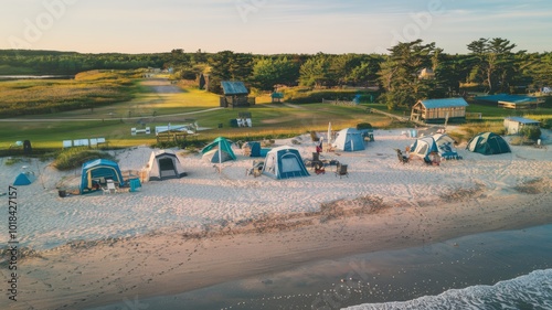 An aerial view of a beachfront campground. There are multiple tents set up on the sandy ground, with some having outdoor furniture.
