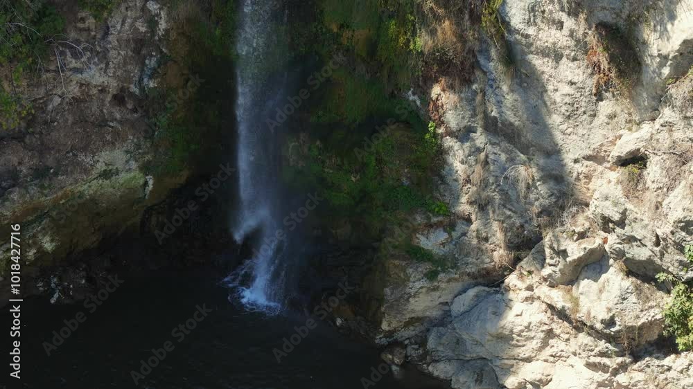Drone, Water Plunges Down From Mossy Cliff Face Into Pool Below. Sunlight Illuminates Scene, Casting Shadows on Rocks. Aerial View Drone, Water Plunges Down From Mossy Cliff Face Into Pool Below. Sunlight Illuminates Scene, Casting Shadows on Rocks. Aerial View
