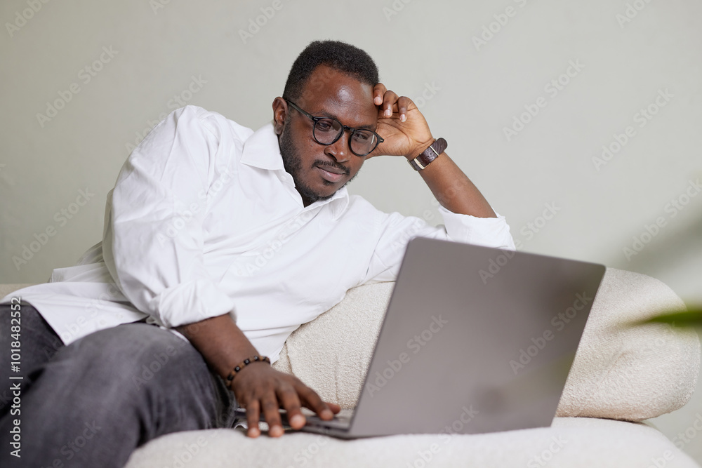 Handsome Black African American Man Working on Laptop Computer while Sitting on a Sofa in Cozy Living Room. Freelancer Working From Home. Browsing Internet, Using Social Networks, Having Fun in Flat. Handsome Black African American Man Working on Laptop Computer while Sitting on a Sofa in Cozy Living Room. Freelancer Working From Home. Browsing Internet, Using Social Networks, Having Fun in Flat.