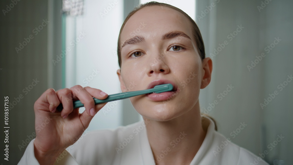 Closeup woman using toothbrush in bathroom setting. Focused girl looking camera Closeup woman using toothbrush in bathroom setting. Focused girl looking camera