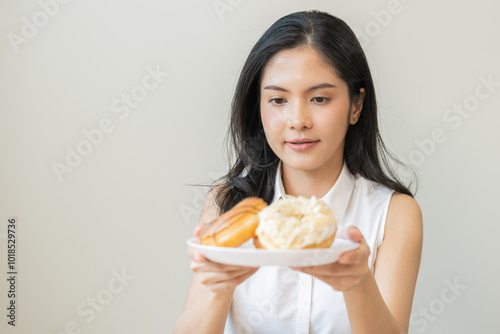 Close up donut plate with happy smile asian young woman, girl temptation food, enjoy eating sugar glazed doughnut and delicious dessert sweet, snack tasty. Eat fast food, junk food meal getting fat.