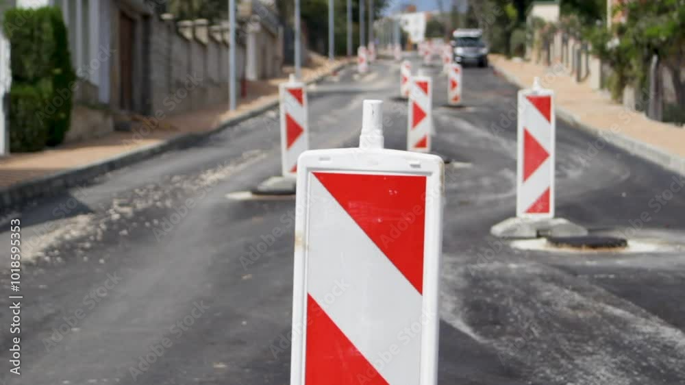 The road after rough asphalt laying with rectangular red and white signs near dangerous areas and manholes. The road after rough asphalt laying with rectangular red and white signs near dangerous areas and manholes.