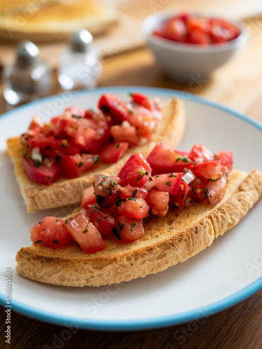 Tasty bruschetta with tomato and onion served on white plate on wooden table 