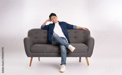 Full body image of young Asian man posing on sofa on white background