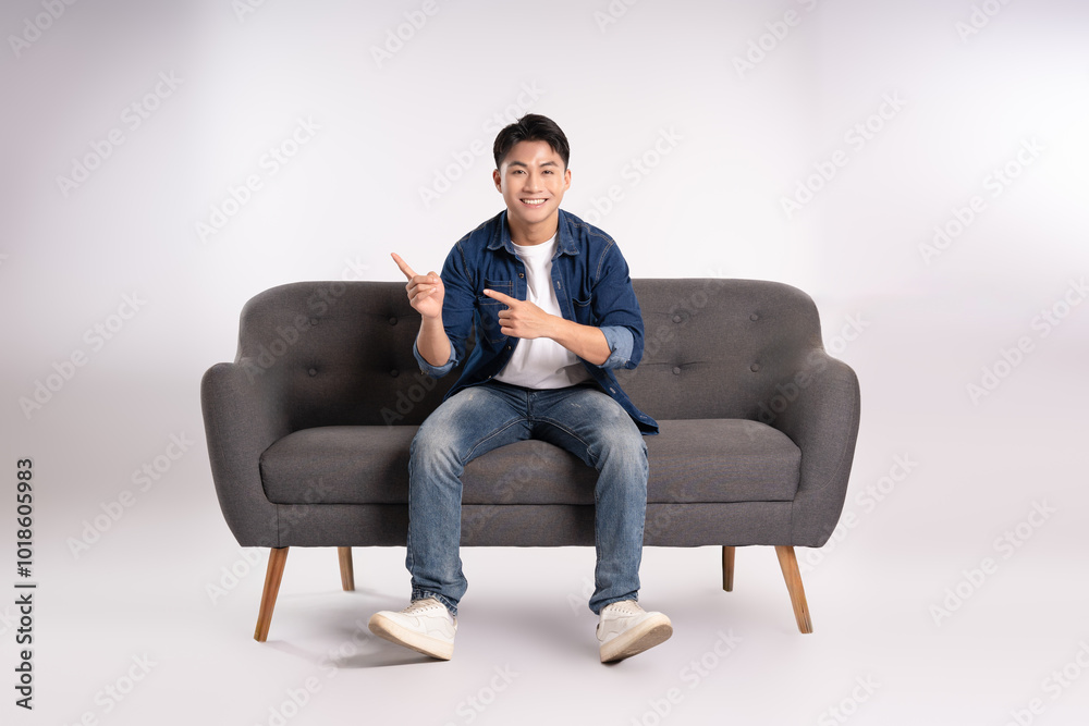 Full body image of young Asian man posing on sofa on white background Full body image of young Asian man posing on sofa on white background
