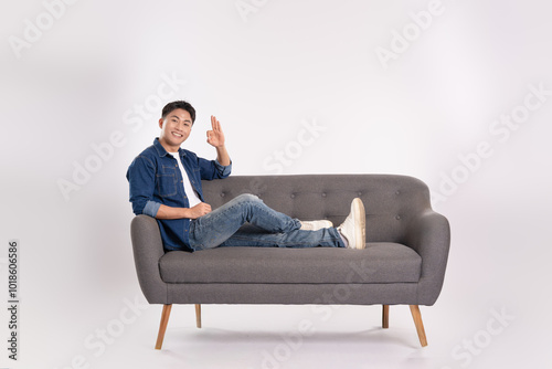 Full body image of young Asian man posing on sofa on white background